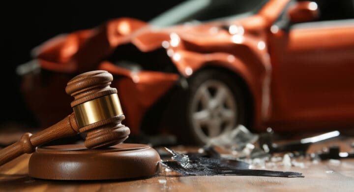 Wooden judge's gavel resting on a sound block in front of a damaged red car after an accident, symbolizing auto accident law and legal proceedings.