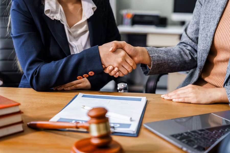 Una abogada y un cliente con traje de negocios se dan la mano después de cerrar con éxito un caso de defensa penal.