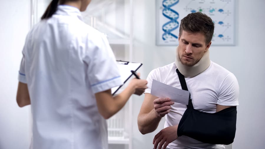 Patient in foam cervical collar and arm sling after accident reading doctors prescription and bills