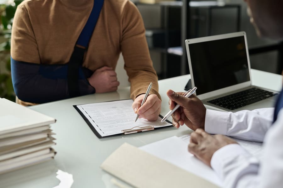 Close up of man filling in medical insurance form, injured hand, and discussing his personal injury case with lawyer