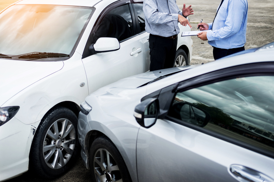 Insurance agent writing on clipboard while examining car after accident claim