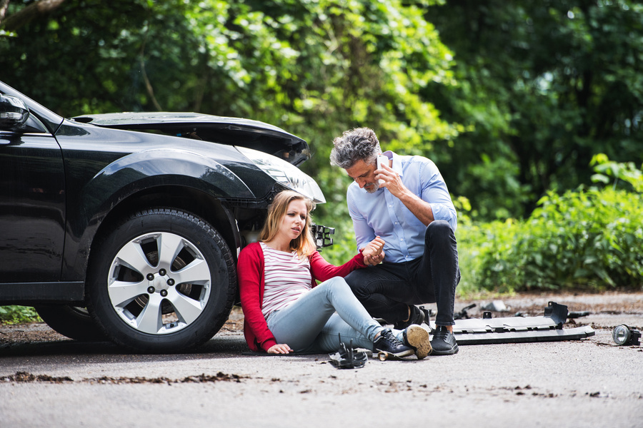 Young woman by the car after an accident and a man with smartphone