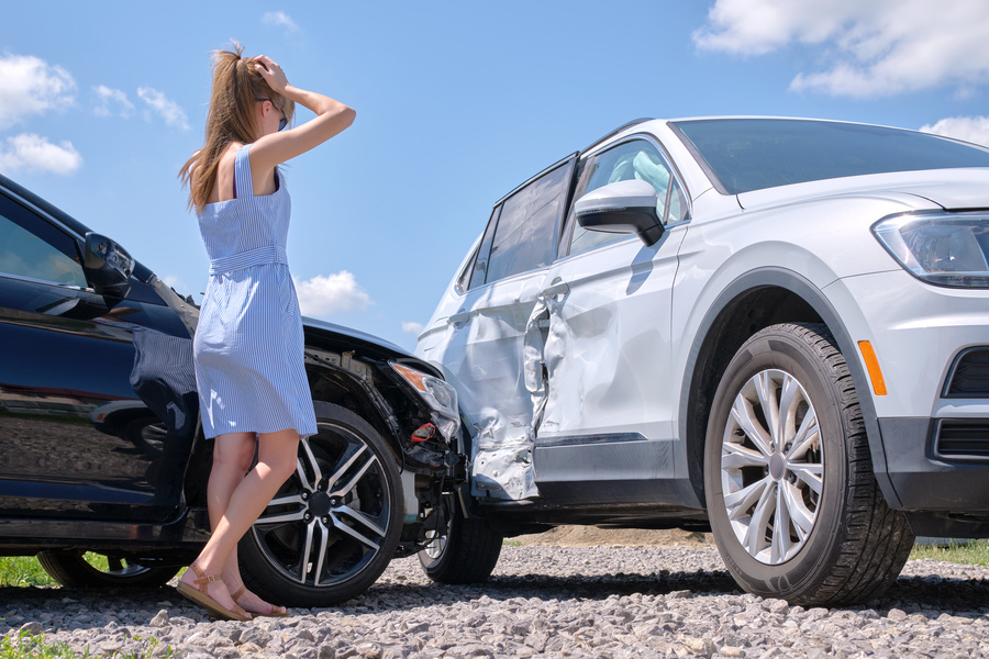 Sad young woman driver standing near her smashed car looking shocked on crashed vehicles in road accident