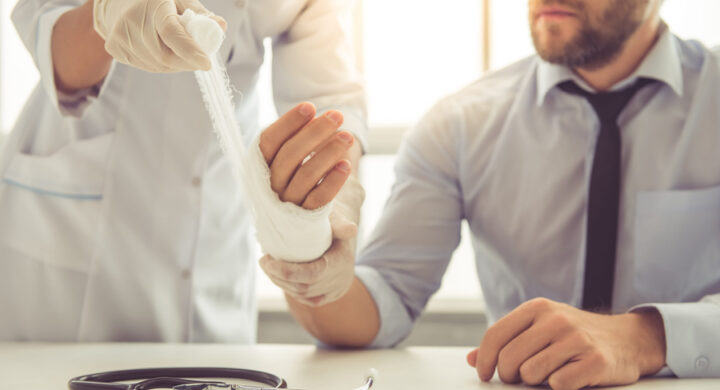 injury after accident - female doctor bandaging man's injured hand