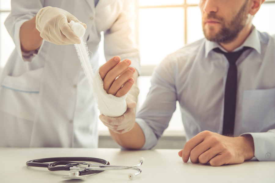 injury after accident - female doctor bandaging man's injured hand