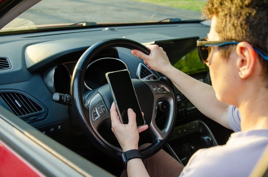 Driver in a car focuses on a smartphone while controlling the steering wheel. This image highlights the risk of distracted driving