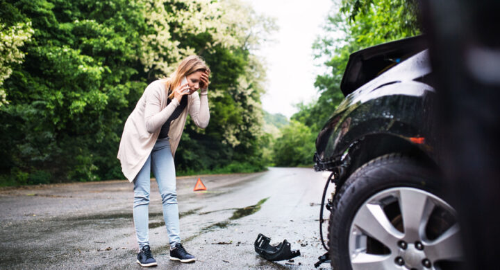 Young woman by the damaged car after a car accident, making a phone call
