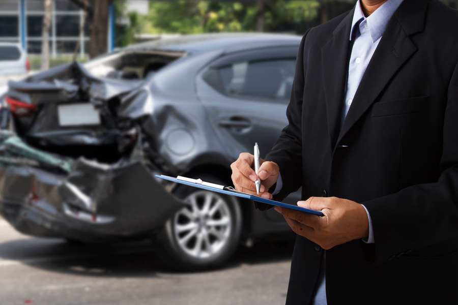 car accident scene - Side view of insurance officer writing on clipboard while insurance agent examining black car after accident.