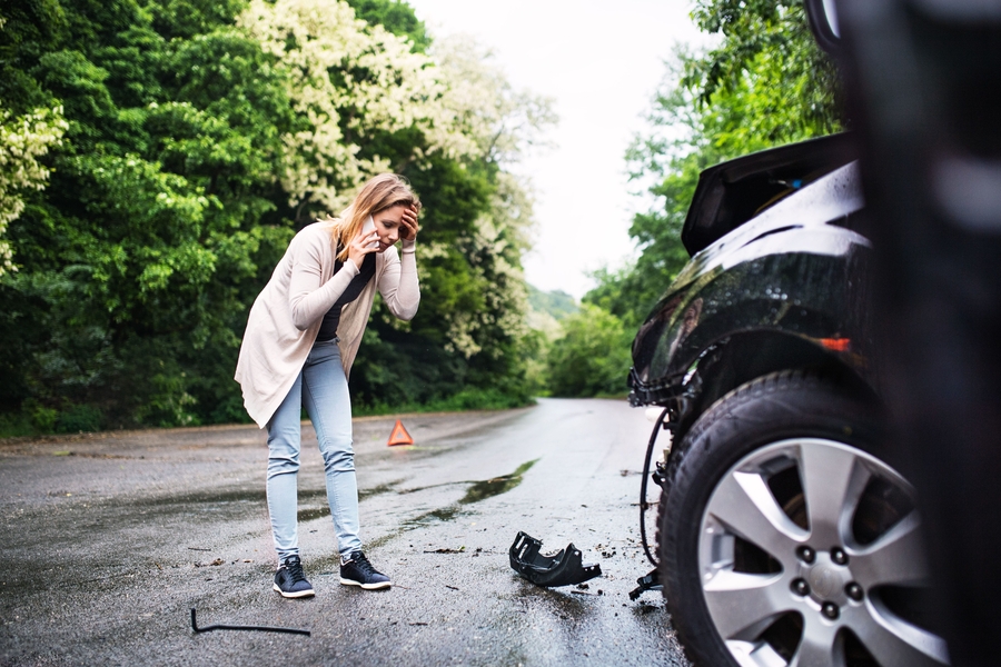 Young woman by the damaged car after a car accident, making a phone call