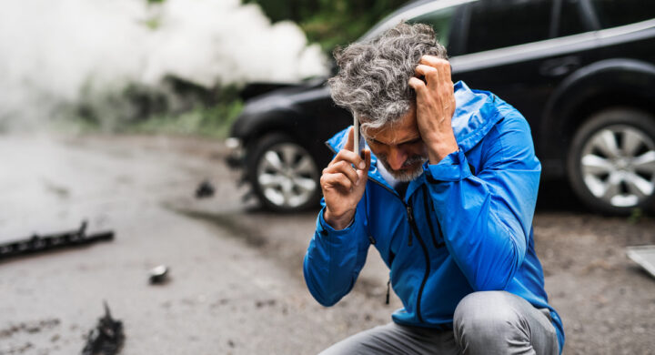 man making a phone call after a car accident, smoke in the background.