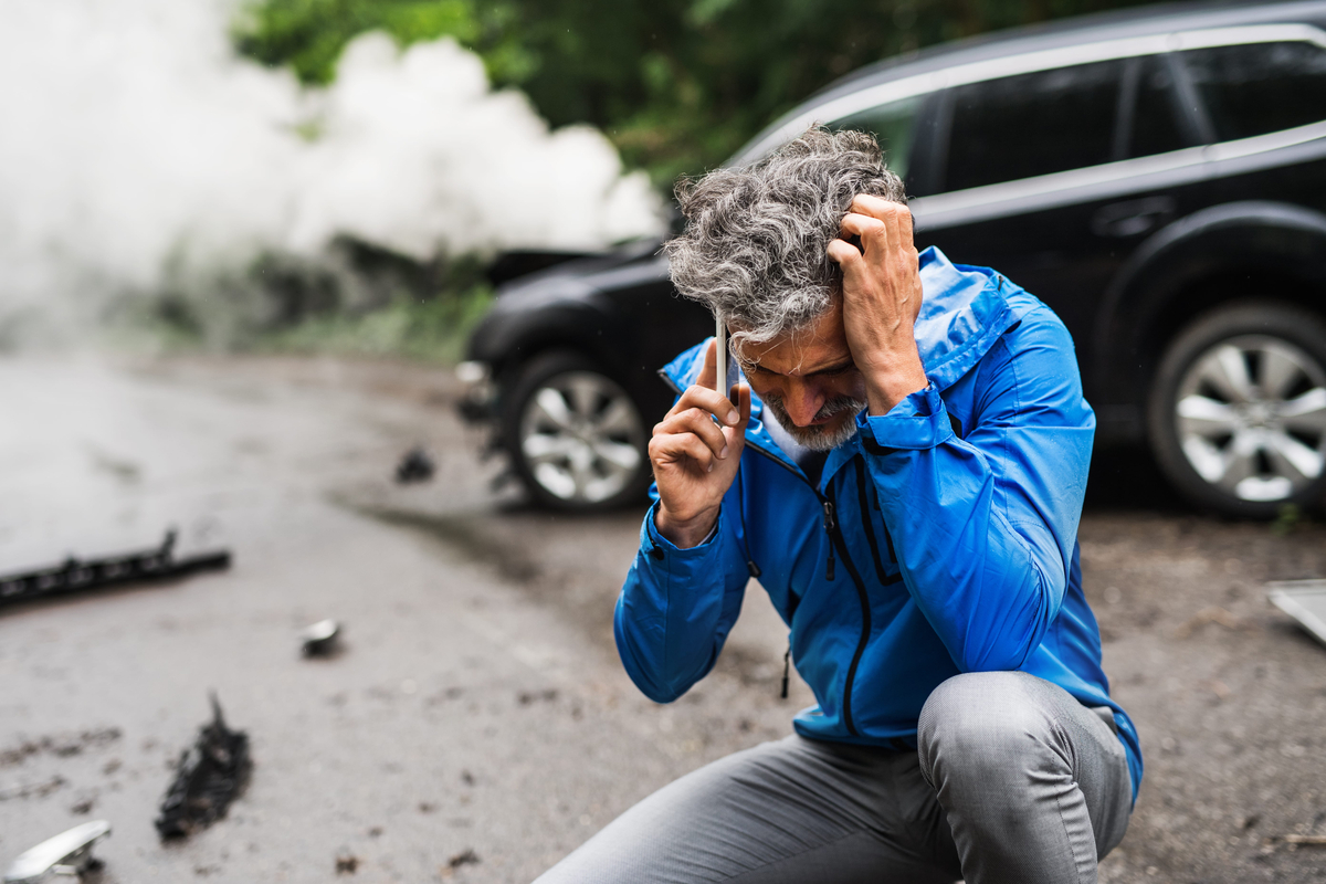 man making a phone call after a car accident, smoke in the background.