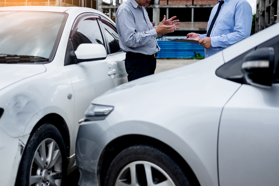 Insurance agent writing on clipboard while examining car after accident claim being assessed and processed